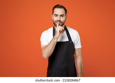 Young Secret Man Barista Bartender Barman Employee In Black Apron White T-shirt Work In Coffee Shop Say Hush Be Quiet Finger On Lips Shhh Gesture Isolated On Orange Background Small Business Startup