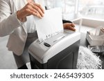 Young secretary destroying paper sheet using shredder in office, closeup