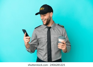 Young security man isolated on blue background holding coffee to take away and a mobile