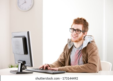 Young Self-confident Office Worker With Nerdy Glasses Smiling At You While Working On His Computer