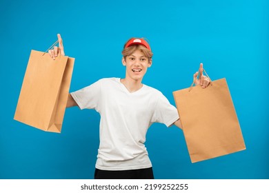 Young Seller In Casual White T-shirt With Paper Bag Isolated On Blue Background Studio Portrait. People Lifestyle Concept. Teen Holding Package Bag With Purchases