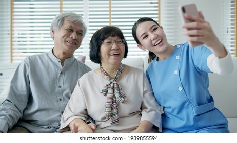 Young Senior Asia Citizen Couple And Assisted Home Living Nurse Care Hold Mobile Phone Selfie Videocall Online At Home Apartment On Sofa Couch In Virtual Digital Telehealth Telemedicine Concept.