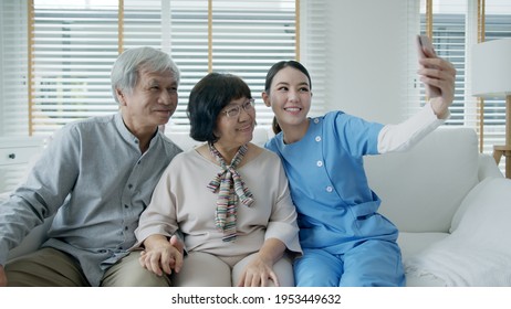 Young Senior Asia Citizen Couple And Assisted Home Living Nurse Care Hold Mobile Phone Selfie Videocall Online At Home Apartment On Sofa Couch In Virtual Digital Telehealth Telemedicine Concept.