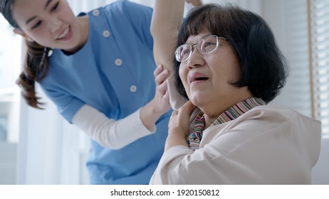 Young Senior Asia Citizen Female With Scrubs Nurse Physiotherapy Worker At Home In Rehabilitation Therapy Service For Aging Parents. Massage For Older Care, Ache Pain Joints Exercise In Old People.