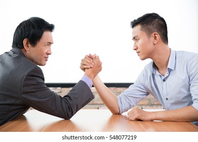 Young and senior businessmen arm-wrestling