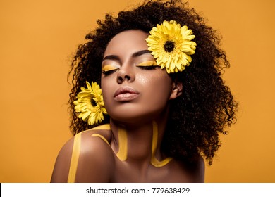 Young sensual african american woman with artistic make-up and gerbera in hair isolated on orange background
