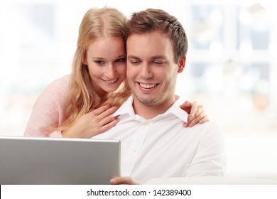 Young Serene Smiling Couple Searching On Internet On Laptop Together In Their Living Room At Home.