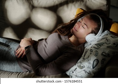 Young Serene Woman Sleeping On Couch In Dark Room While Listening To Relax Music In Headphones