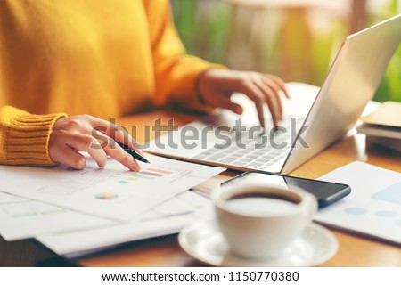 Young serious accountant woman checking paperwork from accounting department to analyse number on document, using laptop check business database, information comparing. Typing keyboard for recording