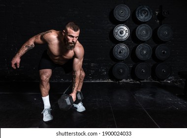 Young serious active sweaty strong fit muscular man with big muscles doing snatch or jerk workout with dumbbell weight in the gym as hardcore cross training real people sport motivation exercising