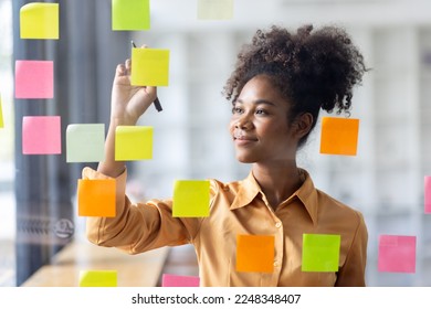Young Serious african american Creative team use post it notes to share idea sticky note on glass wall. Asian business people design planning and Brainstorming thinking sticky History notes concept.
,