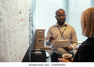 Young Serious African American Male Officer With Documents Consulting With Female Colleague While Matching Facts Of Crime