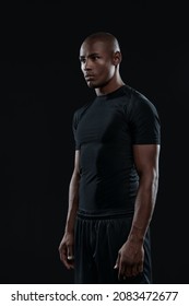 Young Serious Athletic Black Man Standing And Looking Away. Concept Of Healthy Lifestyle. Handsome Muscular Bald Male Person Wearing Sportswear. Isolated On Black Background. Studio Shoot