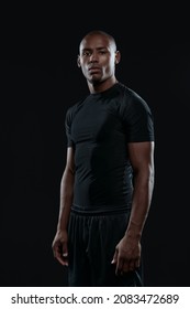 Young Serious Athletic Black Man Standing And Looking At Camera. Concept Of Healthy Lifestyle. Handsome Muscular Bald Male Person Wearing Sportswear. Isolated On Dark Background. Studio Shoot