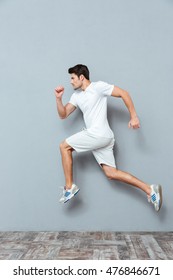 Young Serious Athletic Man Jumping Isolated On The Gray Background