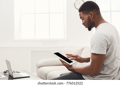 Young Serious Black Man Holding Tablet With Blank Screen On Beige Couch In Light Livingroom At Home, Copy Space, Side View