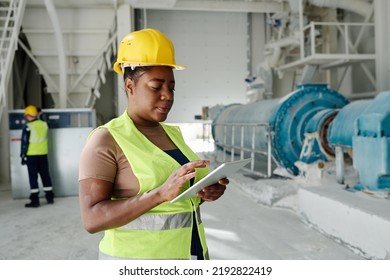 Young Serious Black Woman With Tablet Looking Through Online Technical Data While Standing In Front Of Camera In Workshop Of Factory