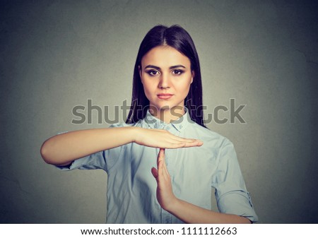 Young serious brunette gesturing for timeout looking at camera confidently while negotiating on gray
