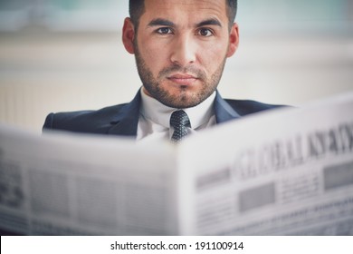 A young serious businessman with newspaper looking at camera