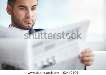 A young serious businessman reading newspaper