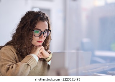 Young serious busy professional business woman employee or student wearing glasses using laptop watching online webinar or training web course, looking at computer, thinking, doing research. - Powered by Shutterstock