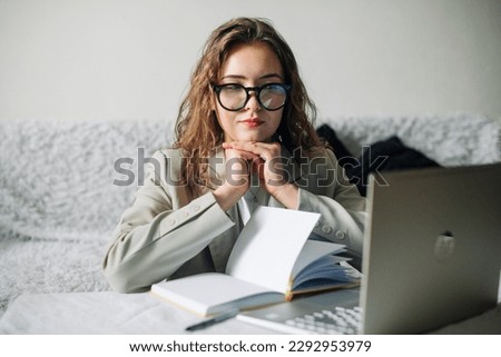 Young serious busy professional businesswoman employee or student wearing glasses using a laptop watching online webinars or training web courses, looking at computers, thinking, and doing research.