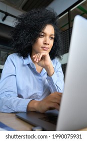 Young Serious Concerned African American Businesswoman Sitting At Desk Looking Laptop Computer In Contemporary Corporation Office. Business Technologies Concept. Vertical Portrait.