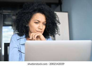 Young serious concerned African American businesswoman sitting at desk looking laptop computer in contemporary corporation office. Business technologies concept. Close up portrait.