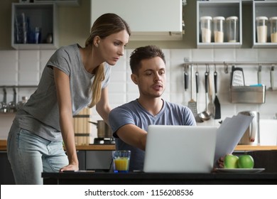 Young Serious Couple Discussing Papers With Laptop, Man And Woman Roommates Or Husband And Wife Checking Rent Or Domestic Bills To Pay Online, Planning Budget Or Analyzing Financial Expenses Together