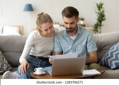 Young Serious Couple Holding Reading Financial Documents Checking Paying Household Bills Online On Laptop, Managing Finances Taxes, Reviewing Bank Accounts, Planning Budget Expenses At Home Together