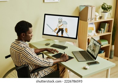 Young serious digital artist with disability looking at laptop screen with graphic picture of warrior while sitting in wheelchair by workplace - Powered by Shutterstock