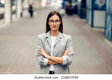 A Young Serious, Elegant Businesswoman Standing On The Street With Arms Crossed And Looking At The Camera. Success Coming With Hard Work. A Young Proud Woman On A Street