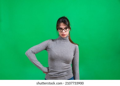 Young Serious Face Bossy Woman With Eyeglasses Not Smiling. Angry Displeased Female Looking At Camera Against Green Not Isolated Background.