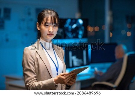 Young serious female programmer or developer in formalwear holding tablet while networking in office environment