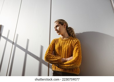 Young serious girl with folded arms stands in front of metal wall and looks to the side