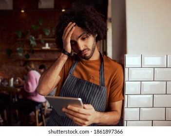 Young Serious Male Cafe Owner Using Digital Tablet While Standing Leaning On Wall