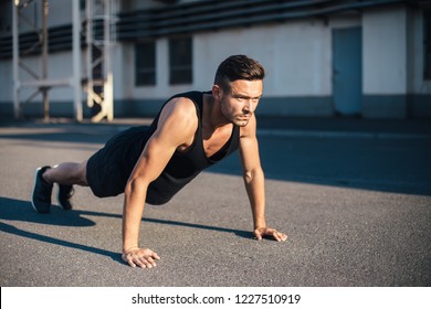 Young serious man doing pushups outdoor on industrial background. concentrated sportsman doing exercise outdoor 