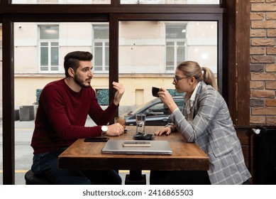 Young serious man having conversation with woman girlfriend sit at cafe table, focused male friend talking to female colleague client solving problem discuss work issues at meeting in coffeehouse - Powered by Shutterstock