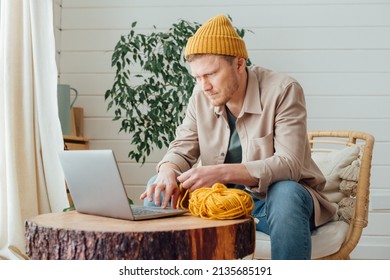 Young Serious Man Looking At Laptop. Man Learning New Hobby, Knitting On Needles. Knitting Project In Progress.