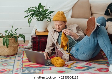 Young Serious Man Looking At Laptop. Man Learning New Hobby, Knitting On Needles. Knitting Project In Progress.