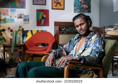 Young Serious Non-binary Man In Trendy Clothes Sitting In Armchair In Front Of Camera While Having Rest In Modern Art Studio