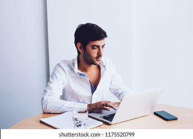 Young Serious Spanish Employer Communicated With Colleague Via Laptop Computer Web Cam Sitting At Office Desktop , Brunette Hair Businessman In White Shirt  Waiting Video Conference On Netbook