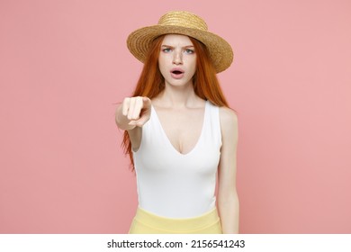 Young serious strict nice redhead woman 20s ginger long hair wearing straw hat summer clothes pointing index finger camera on you opened mouth isolated on pastel pink color background studio portrait