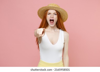 Young serious strict redhead woman 20s ginger long hair wear straw hat summer clothes scream shout point index finger camera on you opened mouth isolated on pastel pink background studio portrait