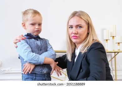 A Young Serious Woman Blonde In A Black Blazer And A Little Boy Portraying A Businessman. Mom Is A Businesswoman With Her Son