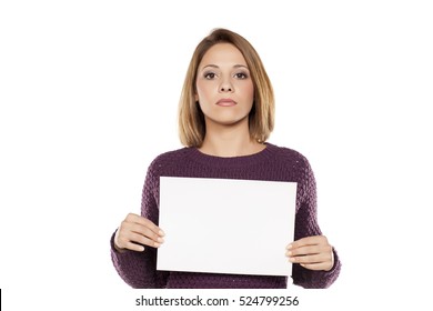 Young Serious Woman Holding A Blank Sheet Of Paper For Advertising