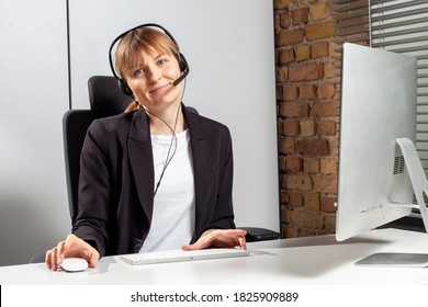 Young Service Employee Sits In Front Of The Monitor With A Headset And Consults Customers By Phone