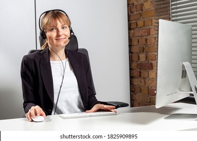 Young Service Employee Sits In Front Of The Monitor With A Headset And Consults Customers By Phone