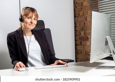 Young Service Employee Sits In Front Of The Monitor With A Headset And Consults Customers By Phone