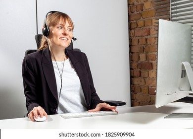 Young Service Employee Sits In Front Of The Monitor With A Headset And Consults Customers By Phone